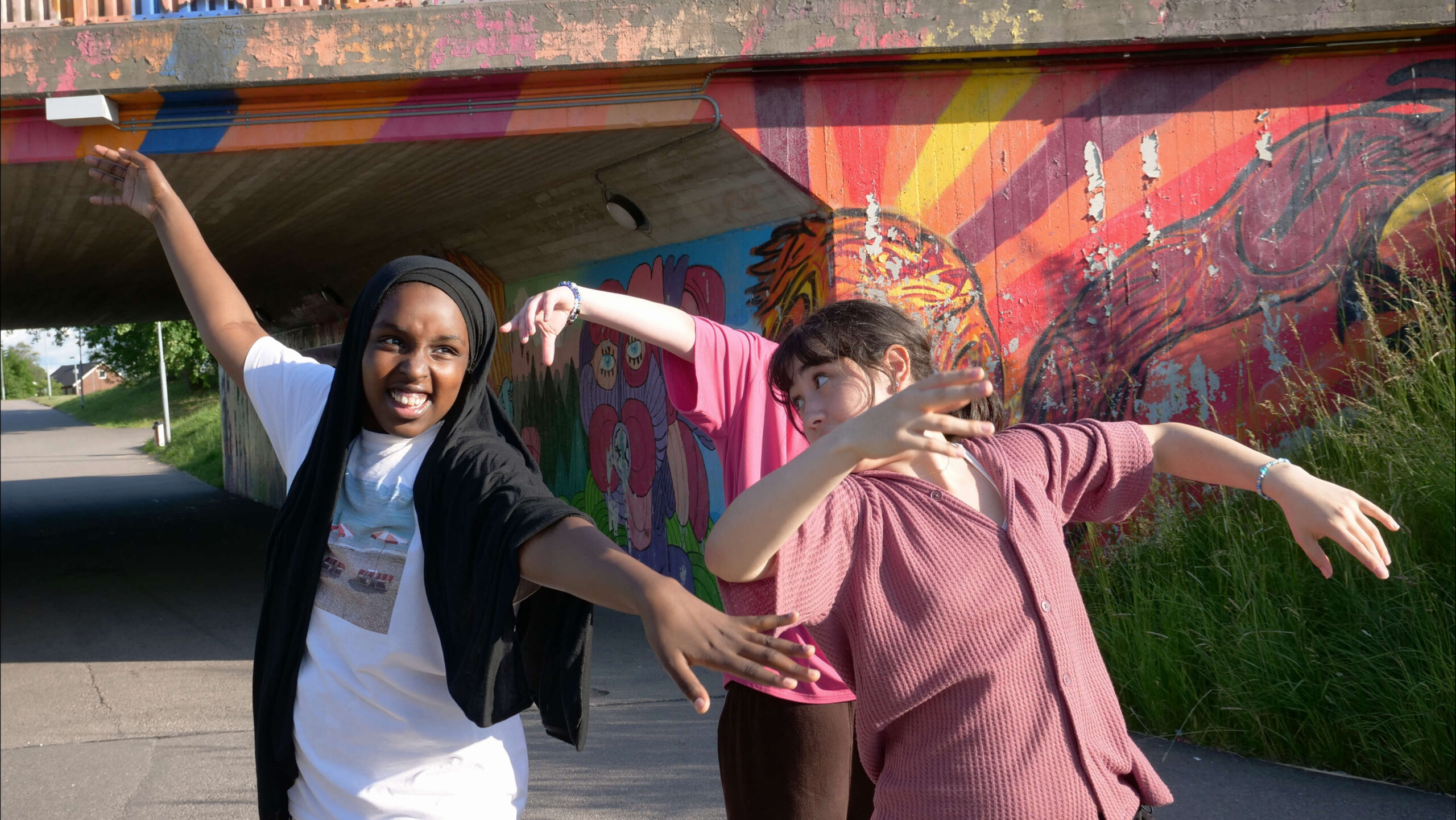 Tre tjejer dansar framför gångtunnel och graffiti
